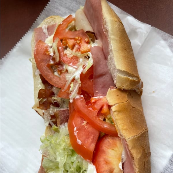 A close-up of a large Anastasia's sub sandwich filled with meat, lettuce, tomatoes, and sauce.