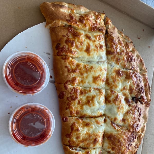 Cheesy garlic breadsticks with two cups of marinara sauce in a pizza box from Anastasia's.