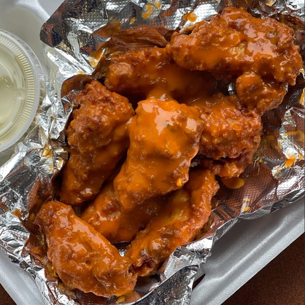 Close-up of Anastasia's Pizza, Oven And Grill's buffalo wings in a foil-lined container with dipping sauce.